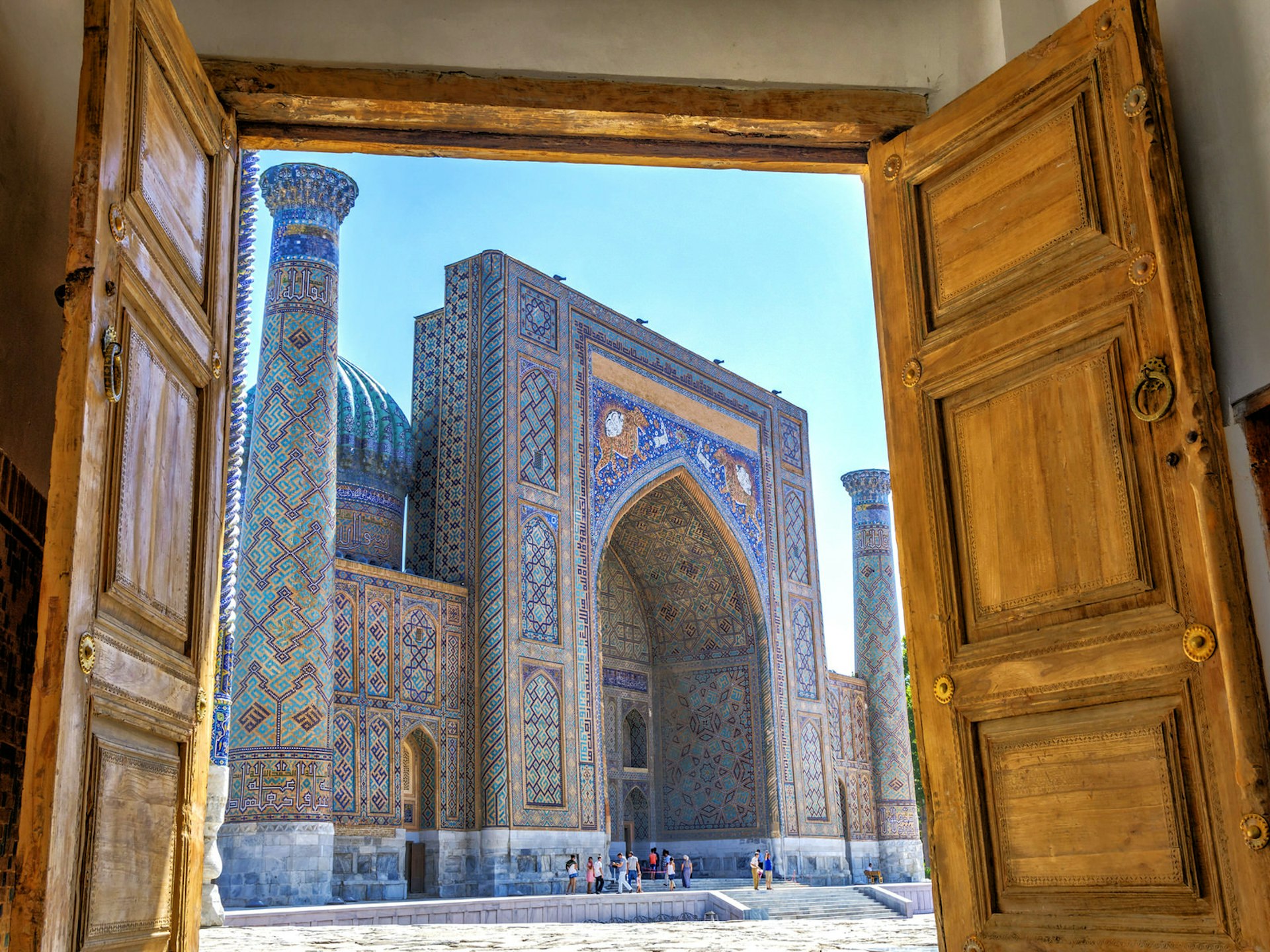 Wooden doors open onto a sunny blue-tiled Islamic square. Uzbekistan's new policies are making it easier to visit its stunning monuments, such as the Registan © Dinozzzaver / Shutterstock