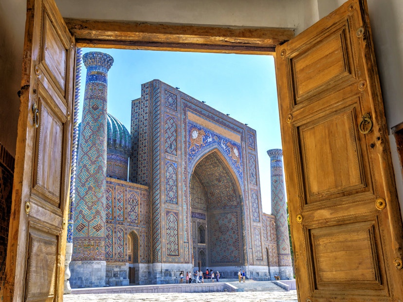 Wooden doors open onto a sunny blue-tiled Islamic square. Uzbekistan's new policies are making it easier to visit its stunning monuments, such as the Registan © Dinozzzaver / Shutterstock