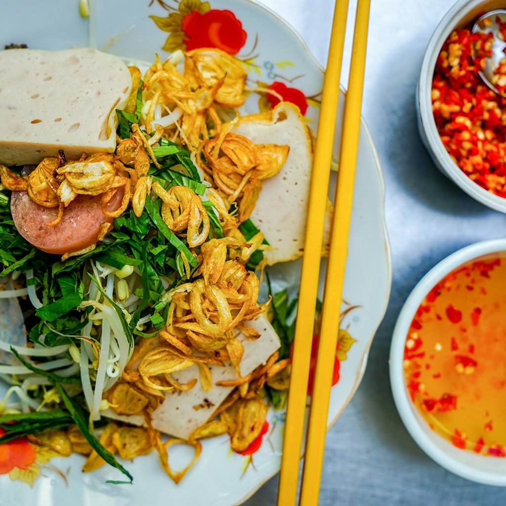 A close-up of a bowl of bánh cuốn, with two small bowls of orange sauces © James Pham / Lonely Planet