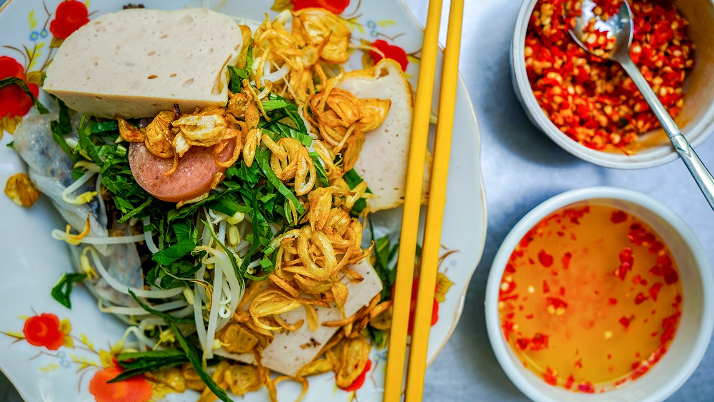 A close-up of a bowl of bánh cuốn, with two small bowls of orange sauces © James Pham / Lonely Planet