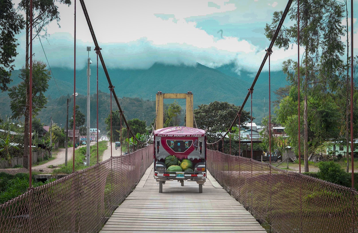 A fruit cart crosses a wooden bridge with misty mountains in the background © Agnes Rivera / Lonely Planet