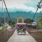 A fruit cart crosses a wooden bridge with misty mountains in the background © Agnes Rivera / Lonely Planet
