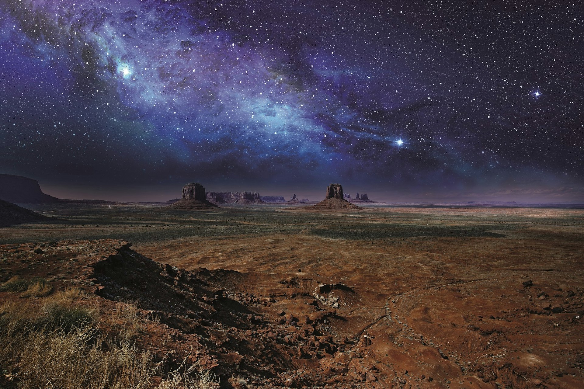 Stars and the milky way stretch over the rock towers of Monument Valley © Claudio Ventrella / Getty Images