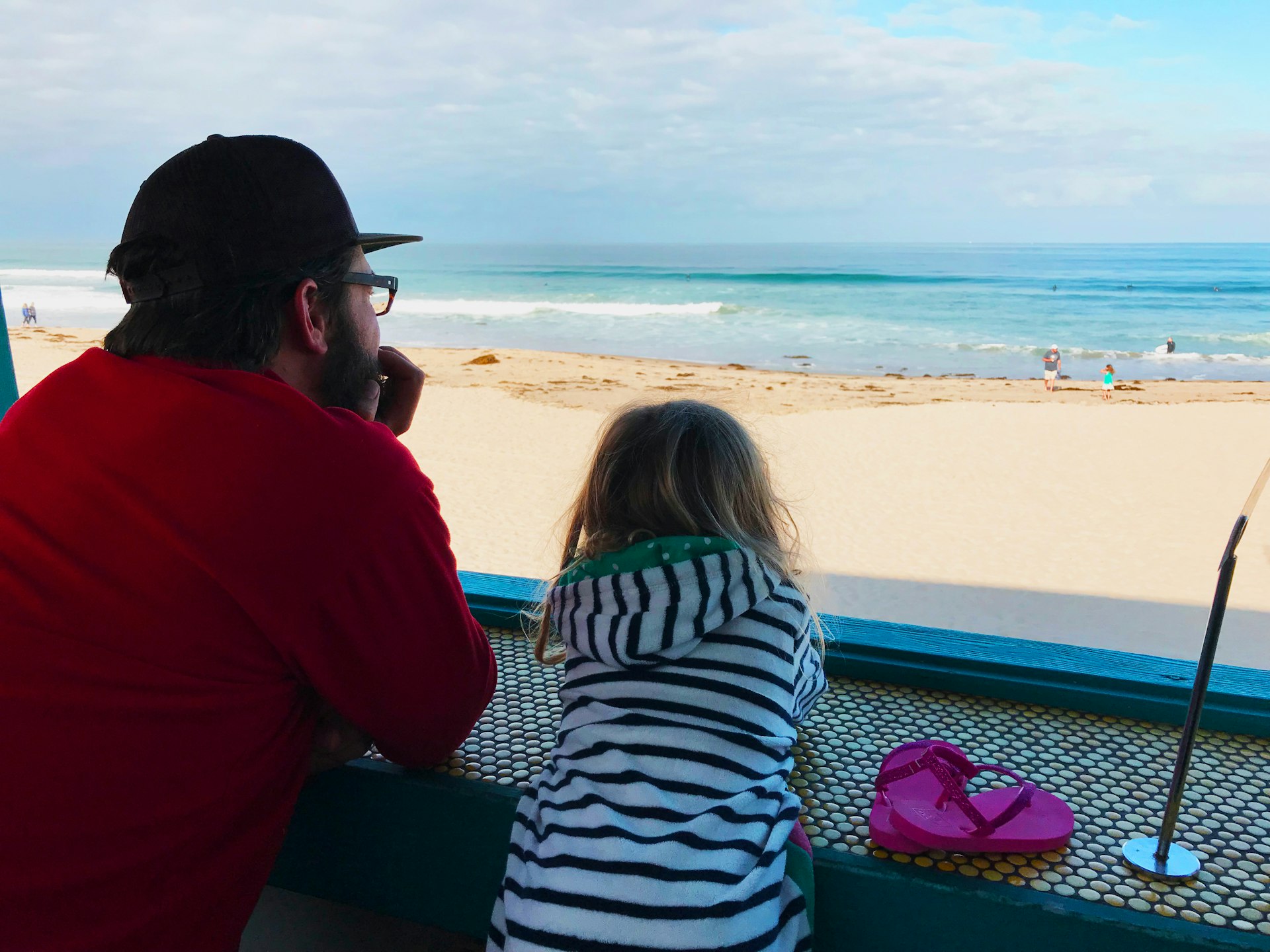 A man and his daughter watch surfers on the beach while waiting for food © Sarah Stocking / Lonely Planet