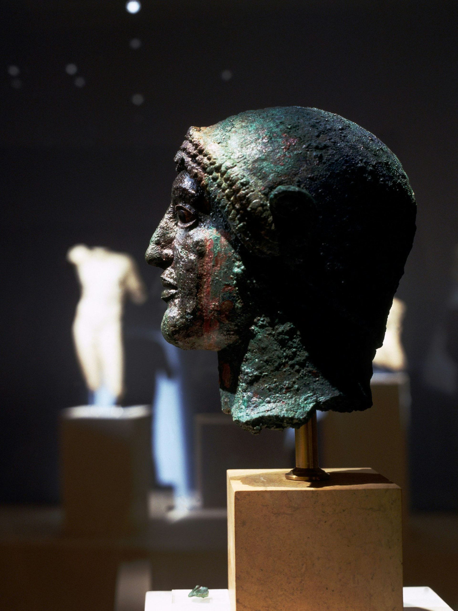 A side angle shot of a bronze head displayed on a plinth