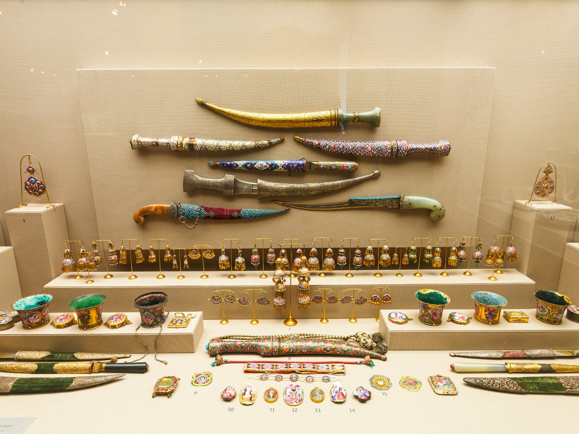 A broad display of jewellery and daggers, many with intricate patterns. Colours are predominantly gold, blue and red