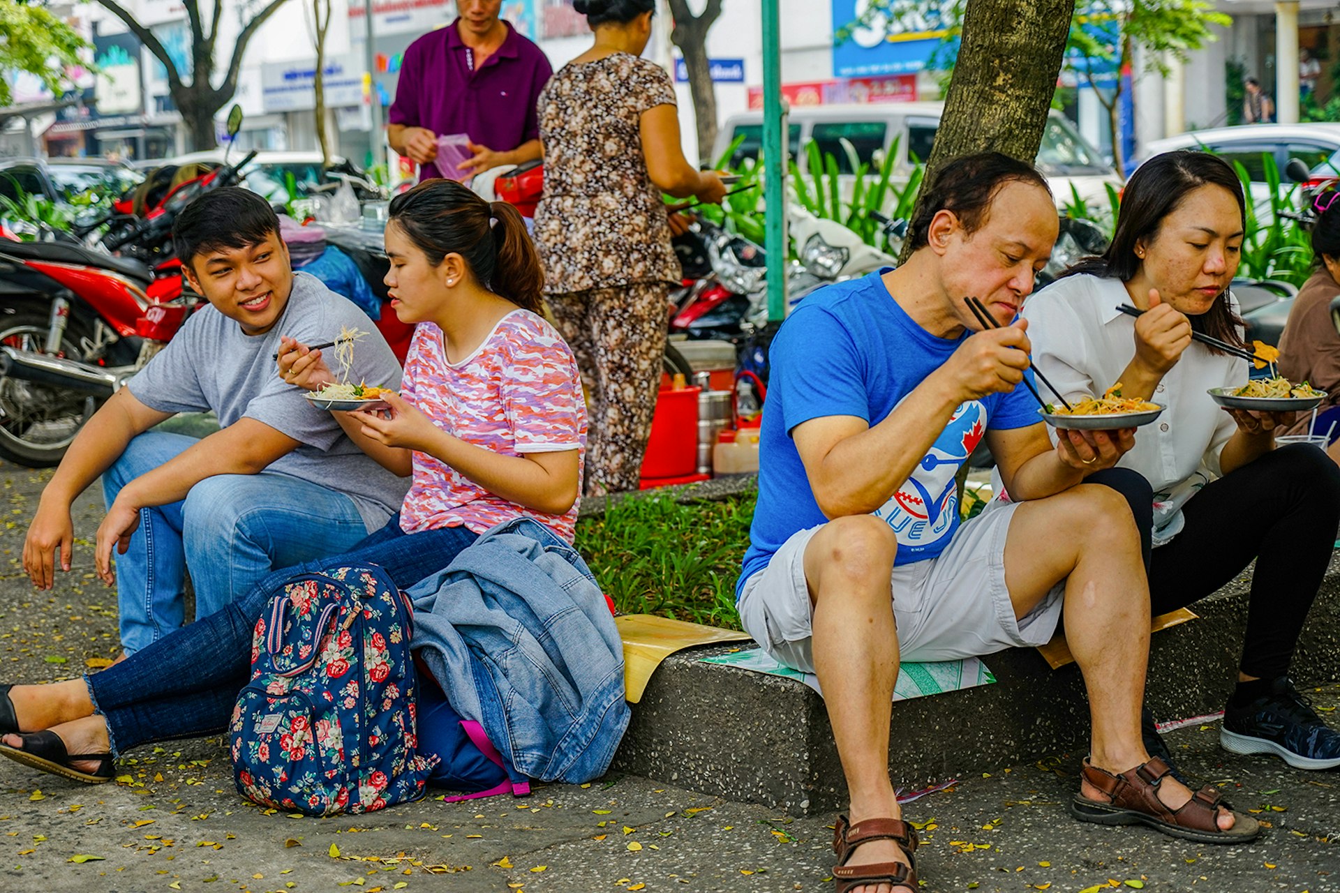People sit on a curb eating plates of papaya salad © James Pham / Lonely Planet
