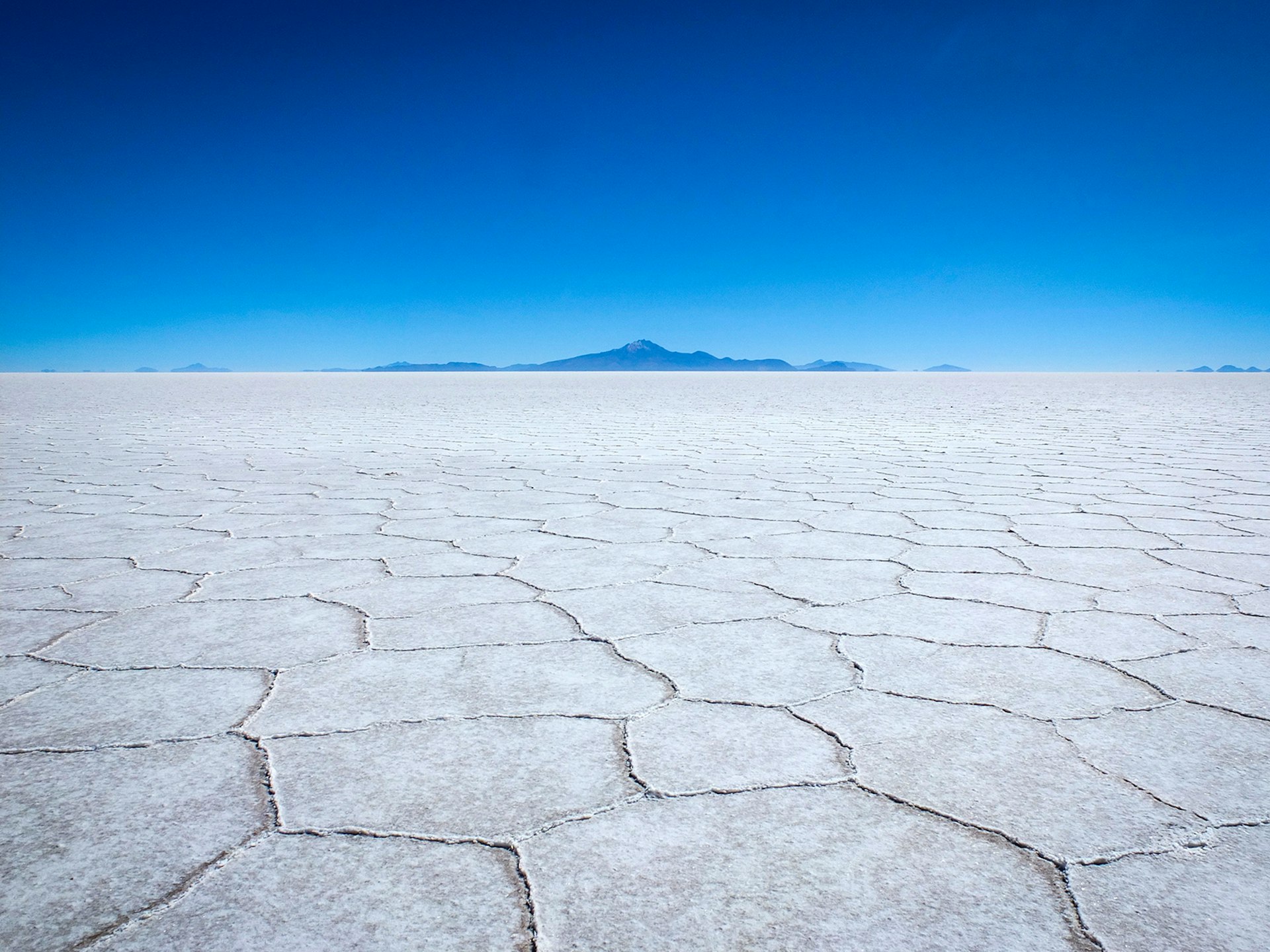 A white salt flat against a blue sky with mountains on the horizon © Sarah Gilbert / Lonely Planet