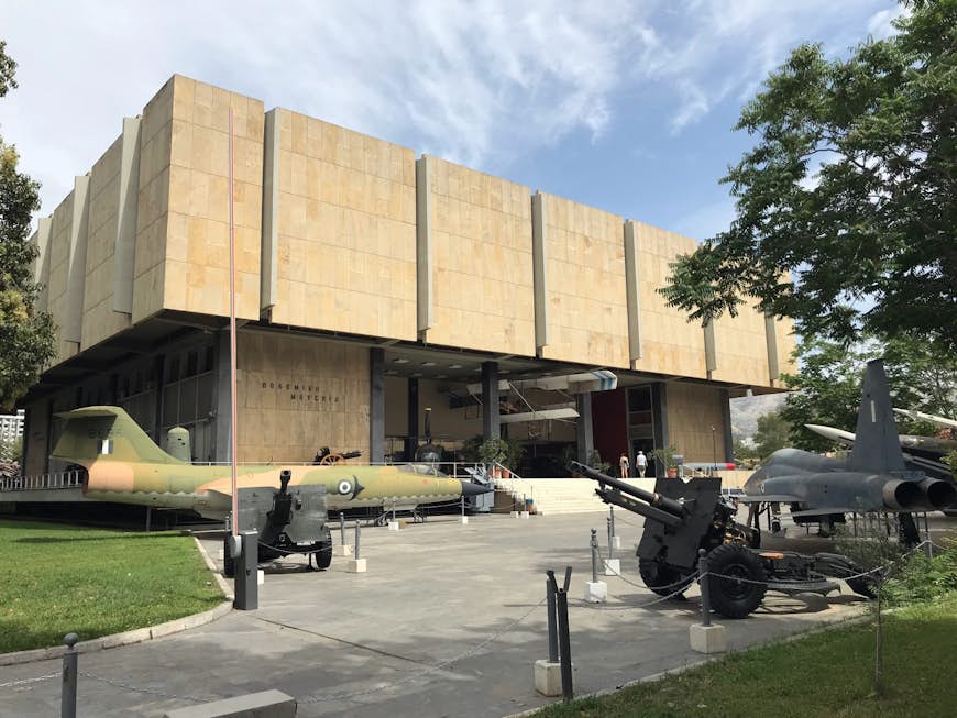 Vintage fighter jets stand outside a square museum building