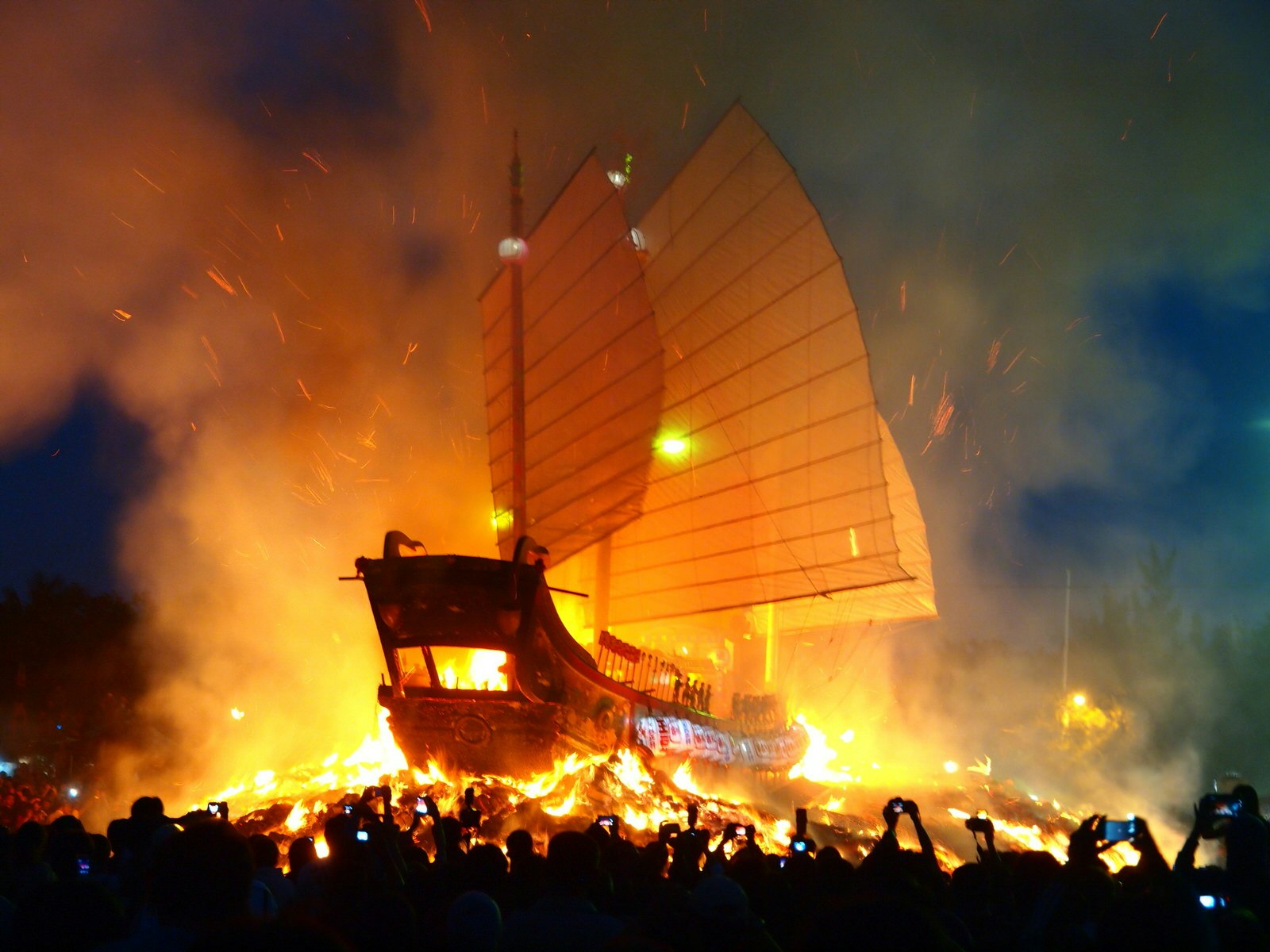 A huge boat with junk sails is set aflame while onlookers hold their phones up to capture the moment. The spectacular Boat Burning Festival takes place around southern Taiwan each autumn to banish demons © 123Nelson / Shutterstock