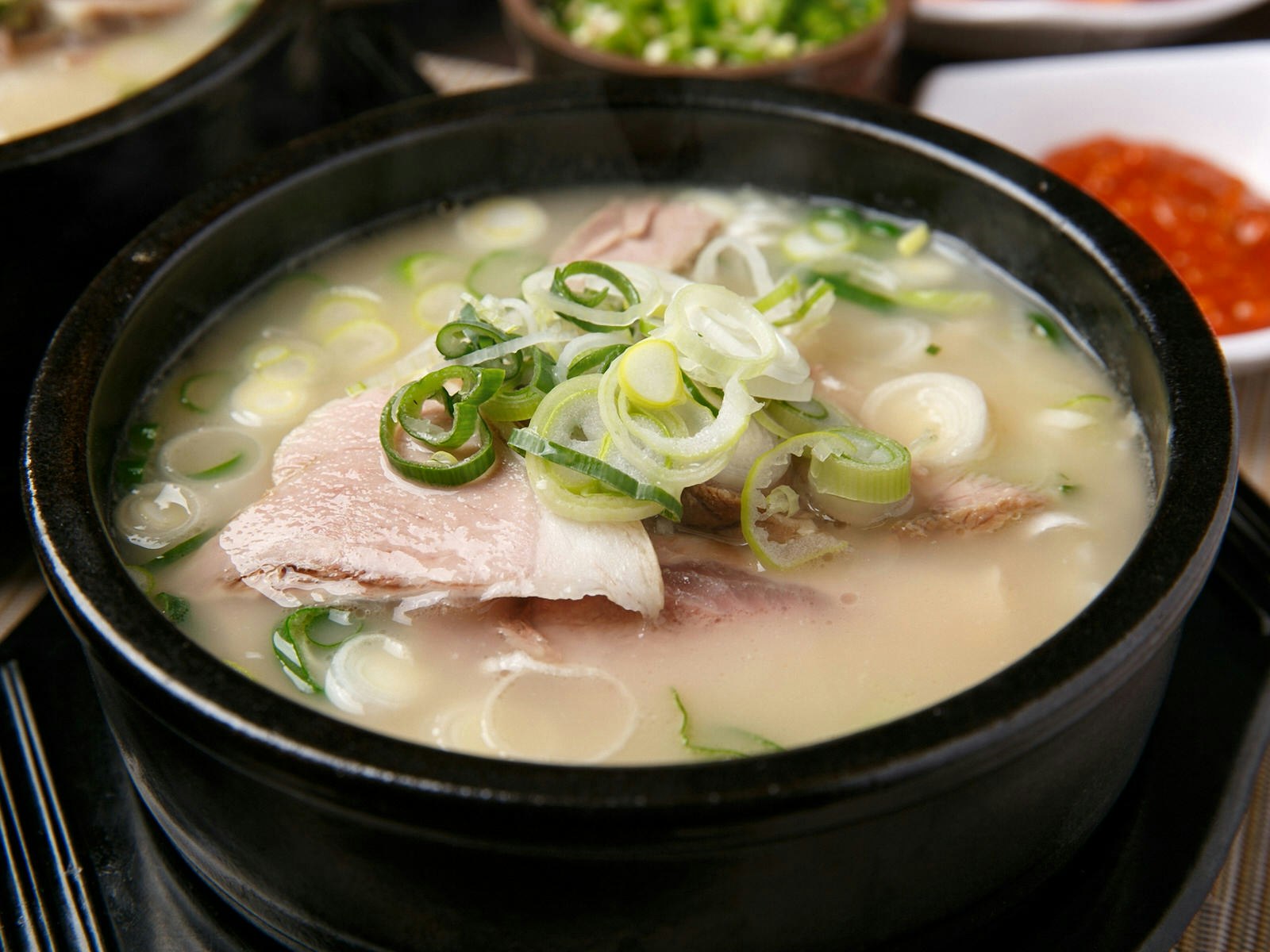 A black bowl of broth with pork slices and green onions on top. Busan's signature dish is dwaeji gukbap, a milky pork broth stew © TMON / Shutterstock