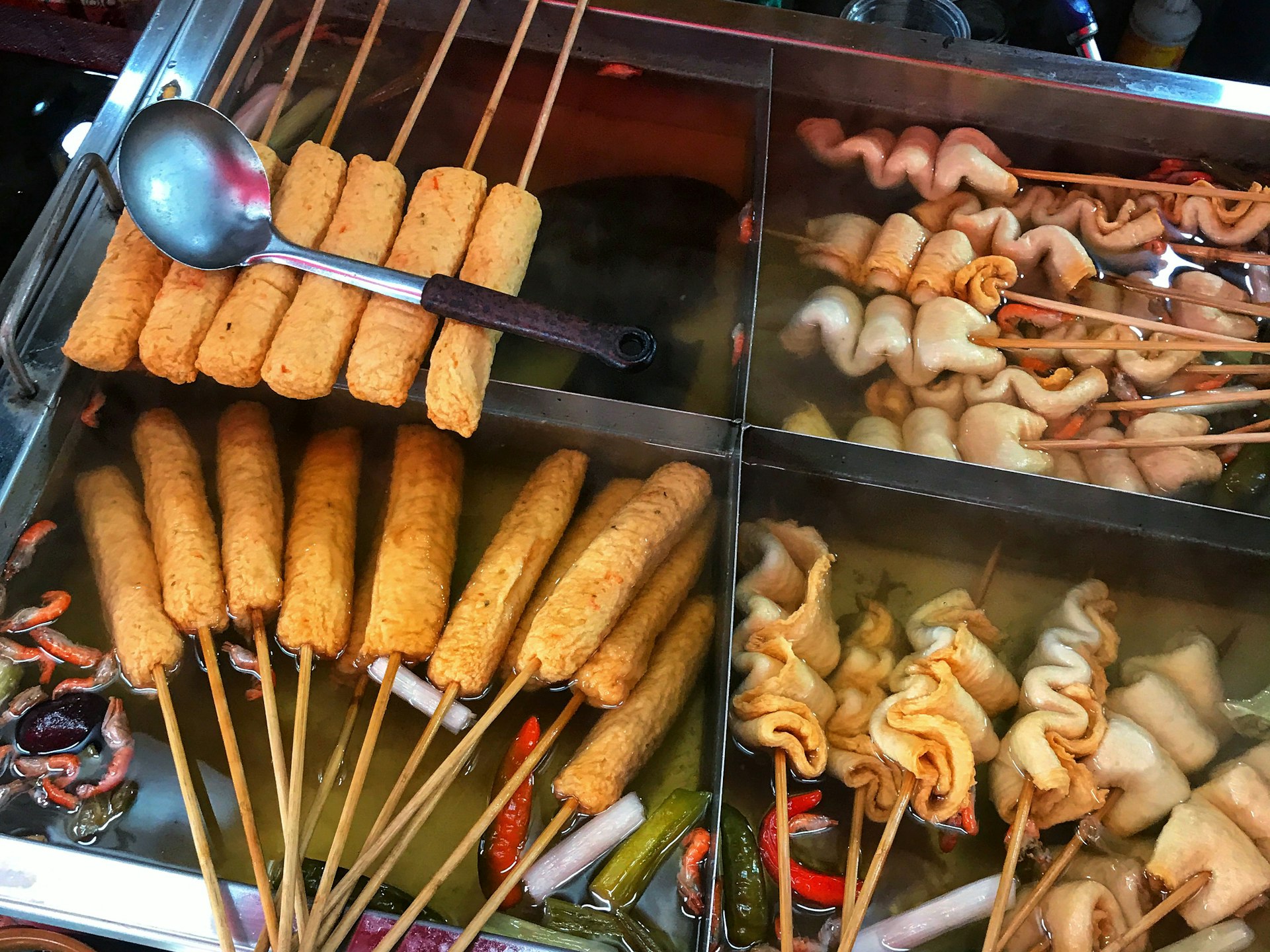 A selection of skewered fishcakes in different shapes sit in boiling pots of broth. Something fishy: eomuk, or fishcakes, are a popular street food in Busan © MaSovaida Morgan / Lonely Planet
