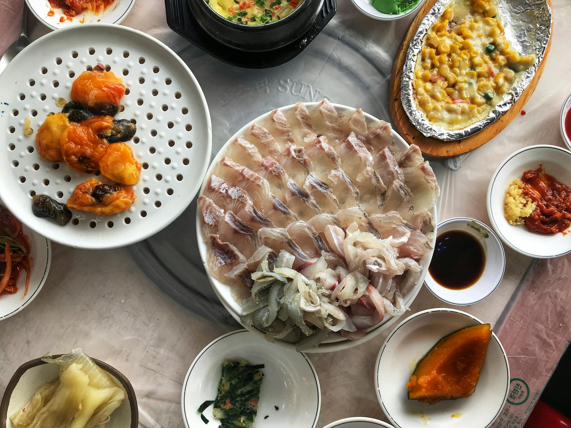 Platters of fish and small bowls of Korean food on a table. Thanks to its oceanside location, Busan's culinary scene is anchored on seafood © MaSovaida Morgan / Lonely Planet