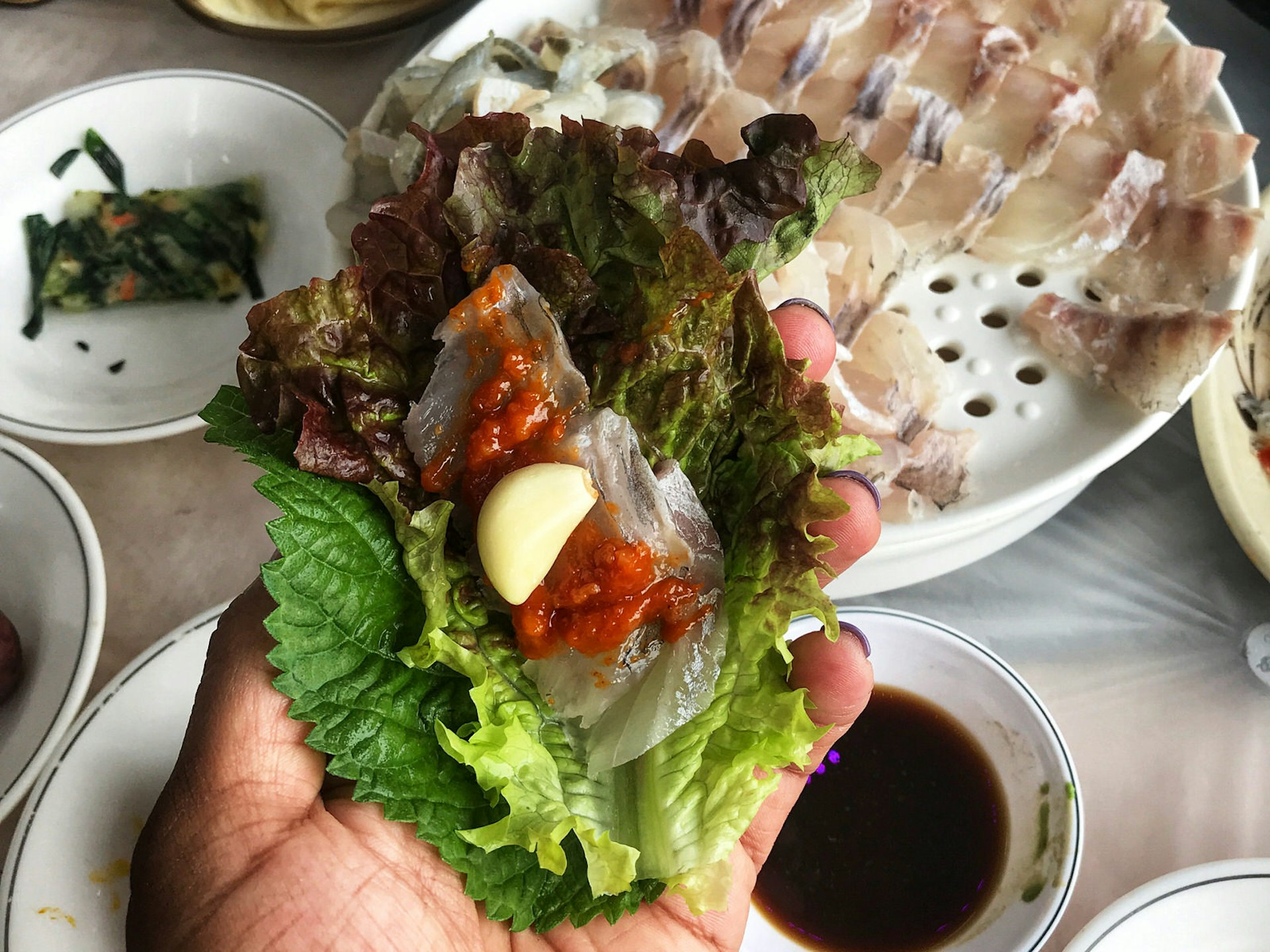 A piece of lettuce topped with raw fish, garlic and red chilli paste. Hoe, or raw seafood, can be enclosed in a piece of lettuce and garnished with sauce and garlic © MaSovaida Morgan / Lonely Planet