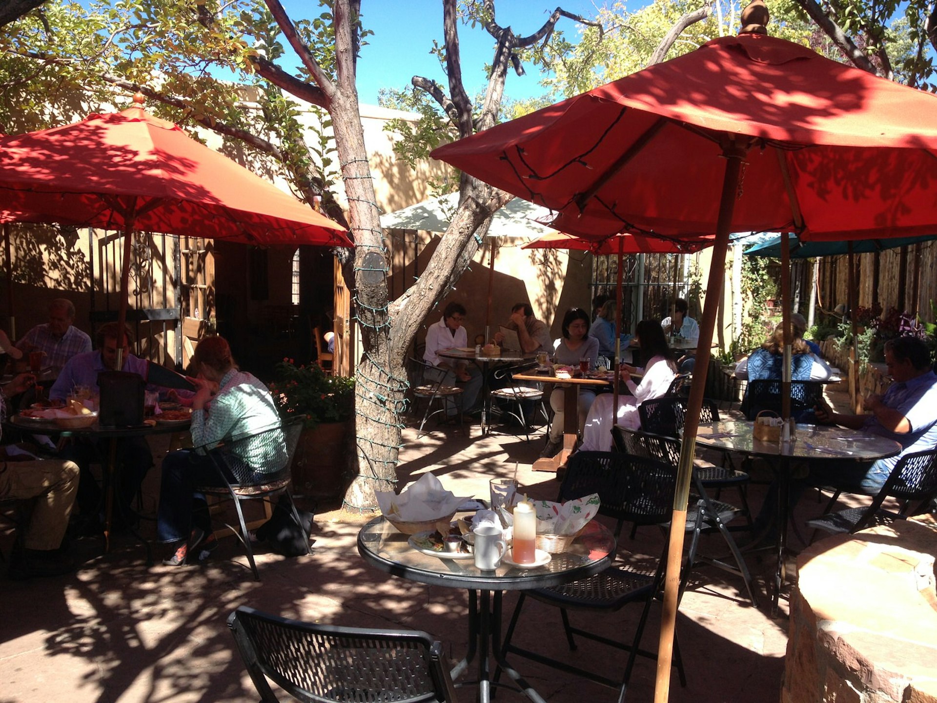 Diners at tables under shade of trees and some red umbrellas. Al fresco dining on the patio (picture: La Choza) is the perfect way to enjoy New Mexico's sunny weather © Megan Eaves / Lonely Planet
