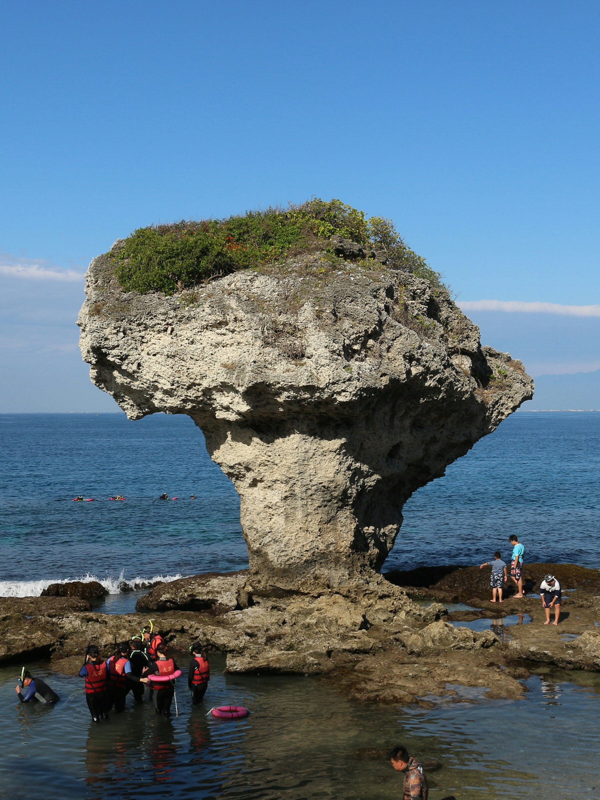 Swimmers and families wade in the shallows around Vase Rock: a coral rock formation formed by sea-level erosion. It is known for its mushroom-like shape. © Piera Chen / Lonely Planet