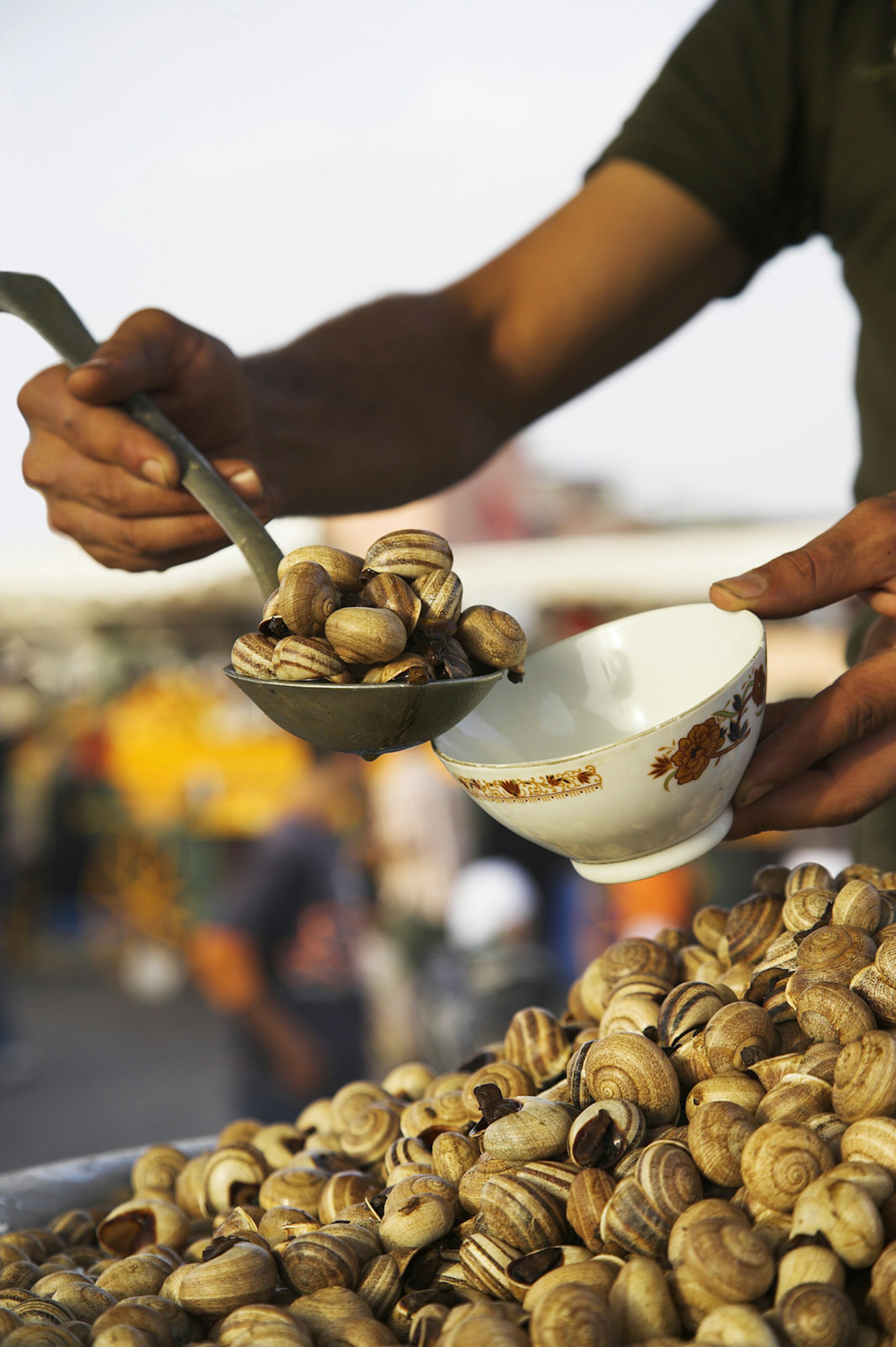 A close up of a vendor's ladle that is full of cooked snails