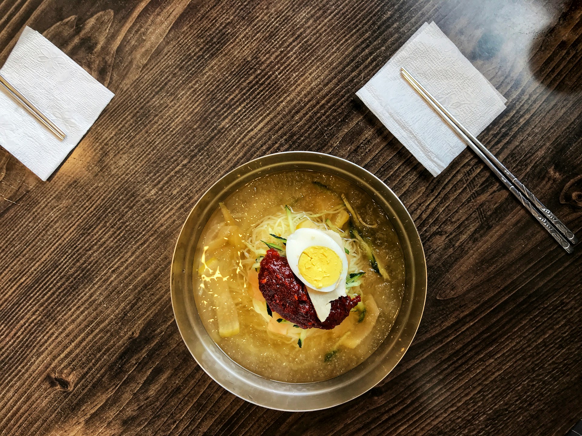 An overhead shot of a bowl with an orange broth topped by a sliced egg and red chilli. Milmyeon: Busan's take on Korean ice noodles with a spicy twist © MaSovaida Morgan / Lonely Planet