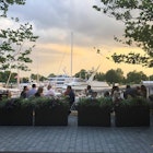 People dine at outdoor tables as the sun sets, with boats parked in the marina behind them © Trisha Ping / Lonely Planet