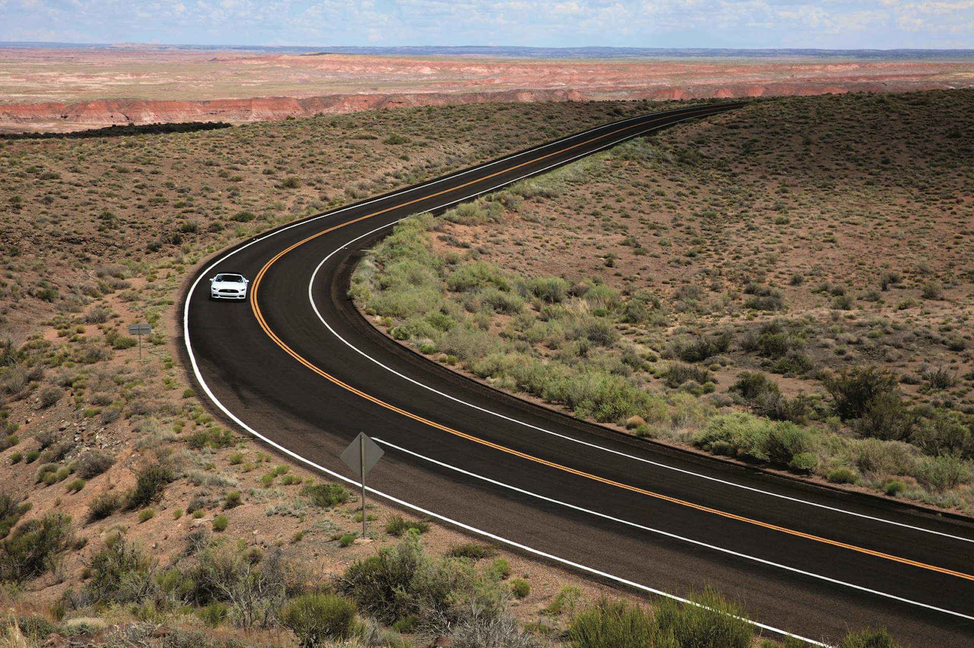 A car drives around a bend in an arid landscape © Paolo Trovo / Shutterstock
