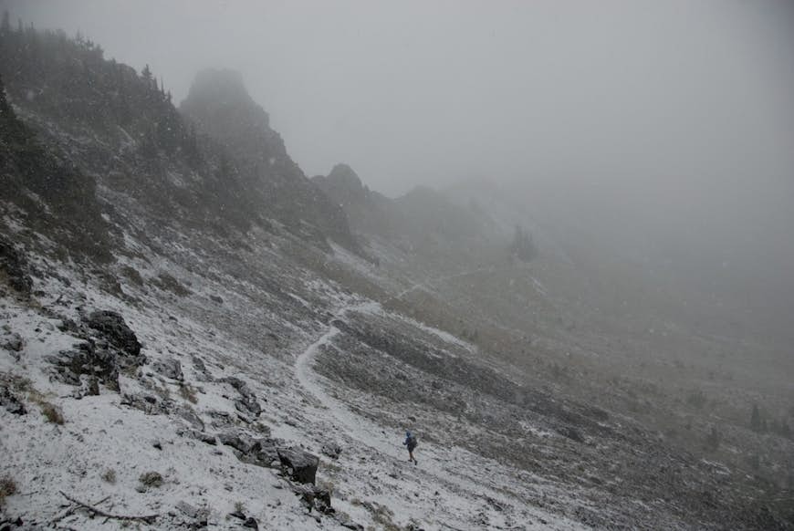 Snö dammar av en ensam del av leden när en ensam vandrare tar sig igenom ett bergspass höljt i dimma på Pacific Crest Trail © Sean Jansen / Lonely Planet 