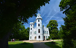 Berlin day trips - Pfaueninsel Palace on Pfaueninsel, which means 'Peacock Island' in german. The palace is white with two turrets and sits amid leafy green trees against a clear blue sky