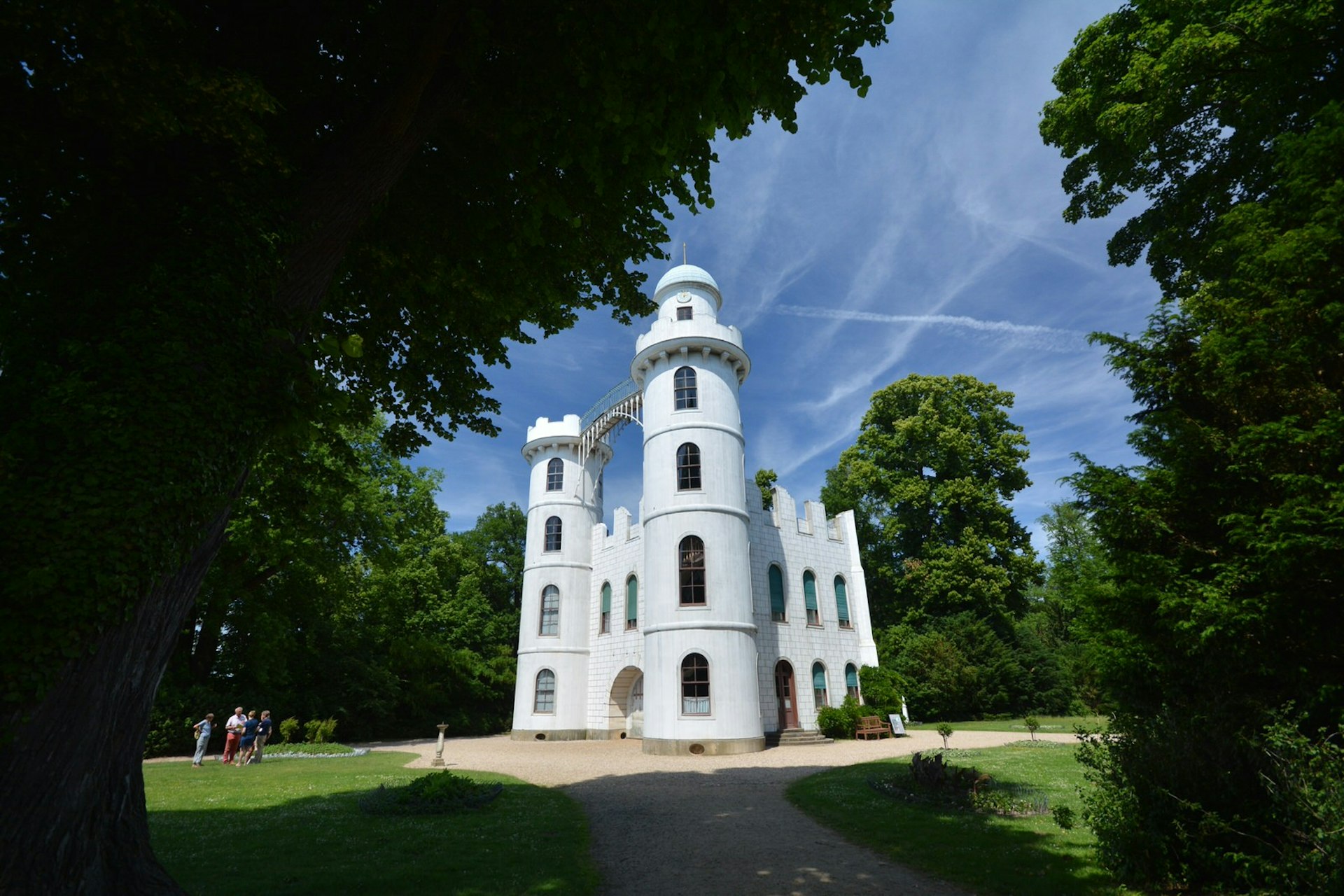 Berlin day trips - Pfaueninsel Palace on Pfaueninsel, which means 'Peacock Island' in German. The palace is white with two turrets and sits amid leafy green trees against a clear blue sky