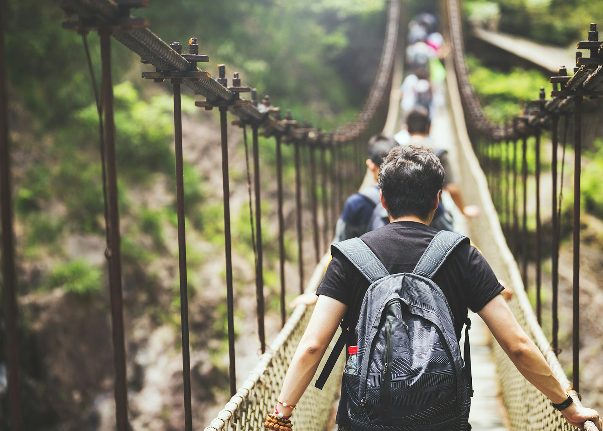 A group of travellers walking over a suspension bridge in the jungle © Qi Yang / Getty Images