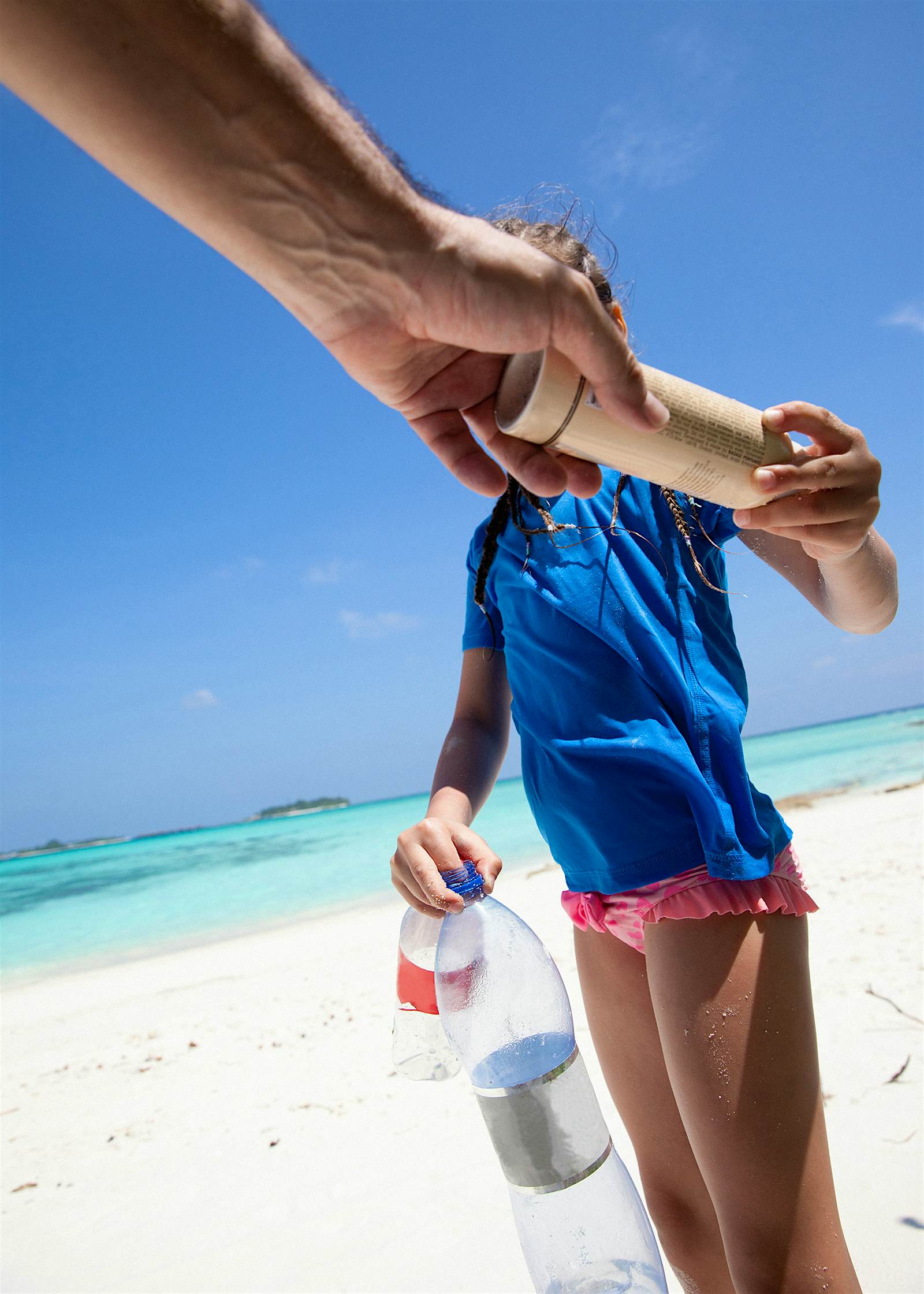 Features - Young Girl Picking Up Plastic Bottles on Beach and Giving Them to Her Father A young girl picking up plastic bottles on a beach and giving them to her father © CasarsaGuru / Getty Images