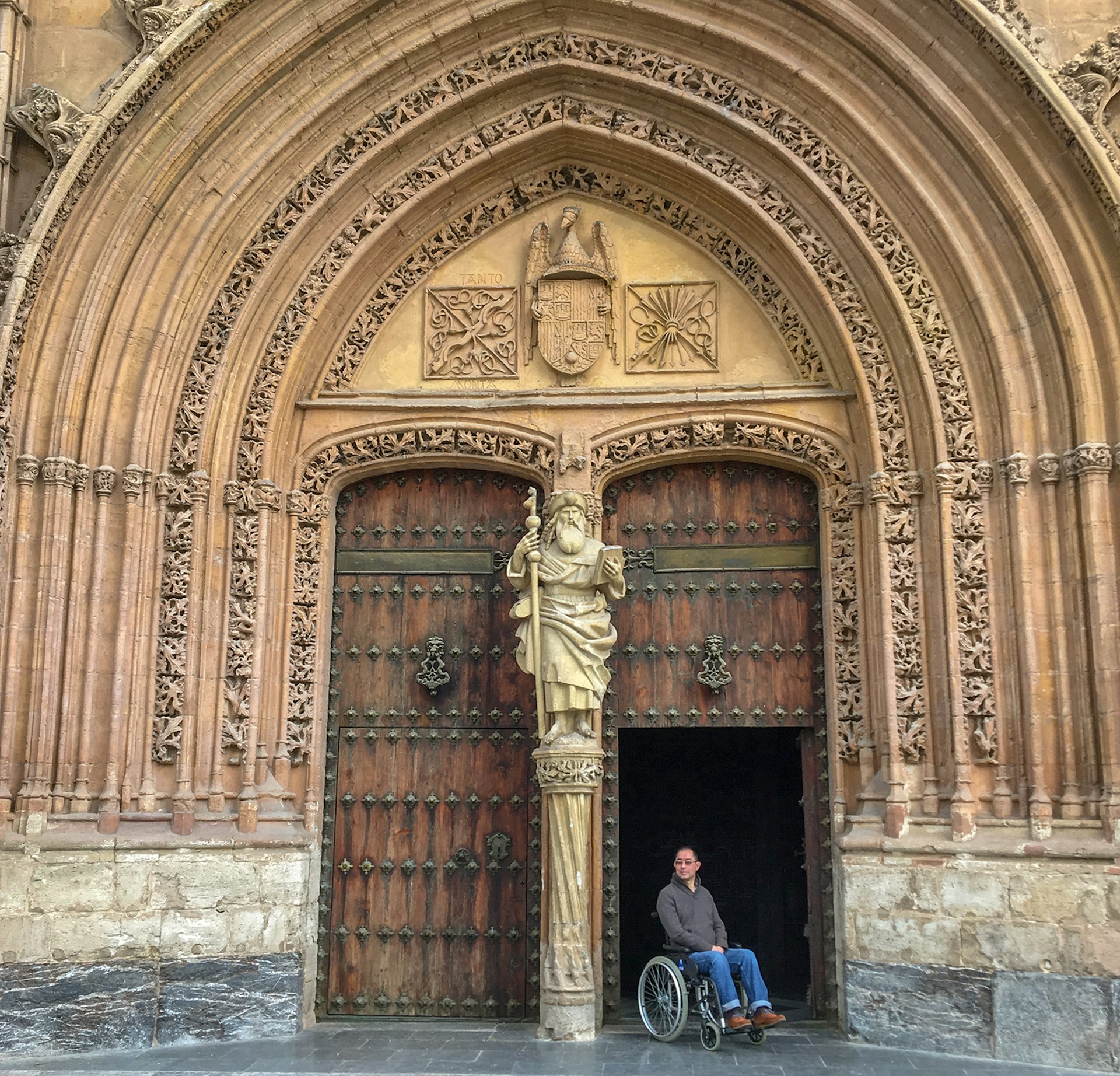A man in a wheelchair in front of an ornately decorated cathedral entrance © Martin Heng