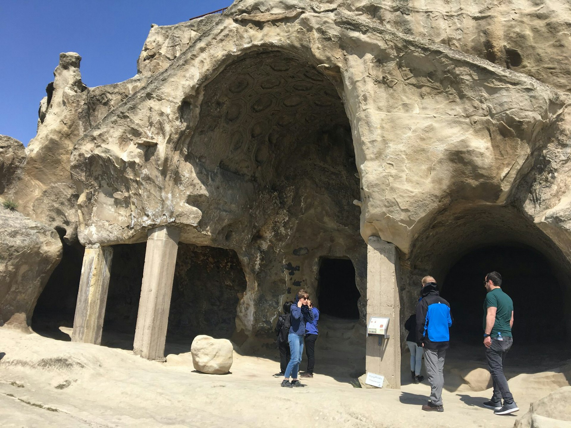 A large archway and pillars supporting a cave structure. Several people are standing near the entrance