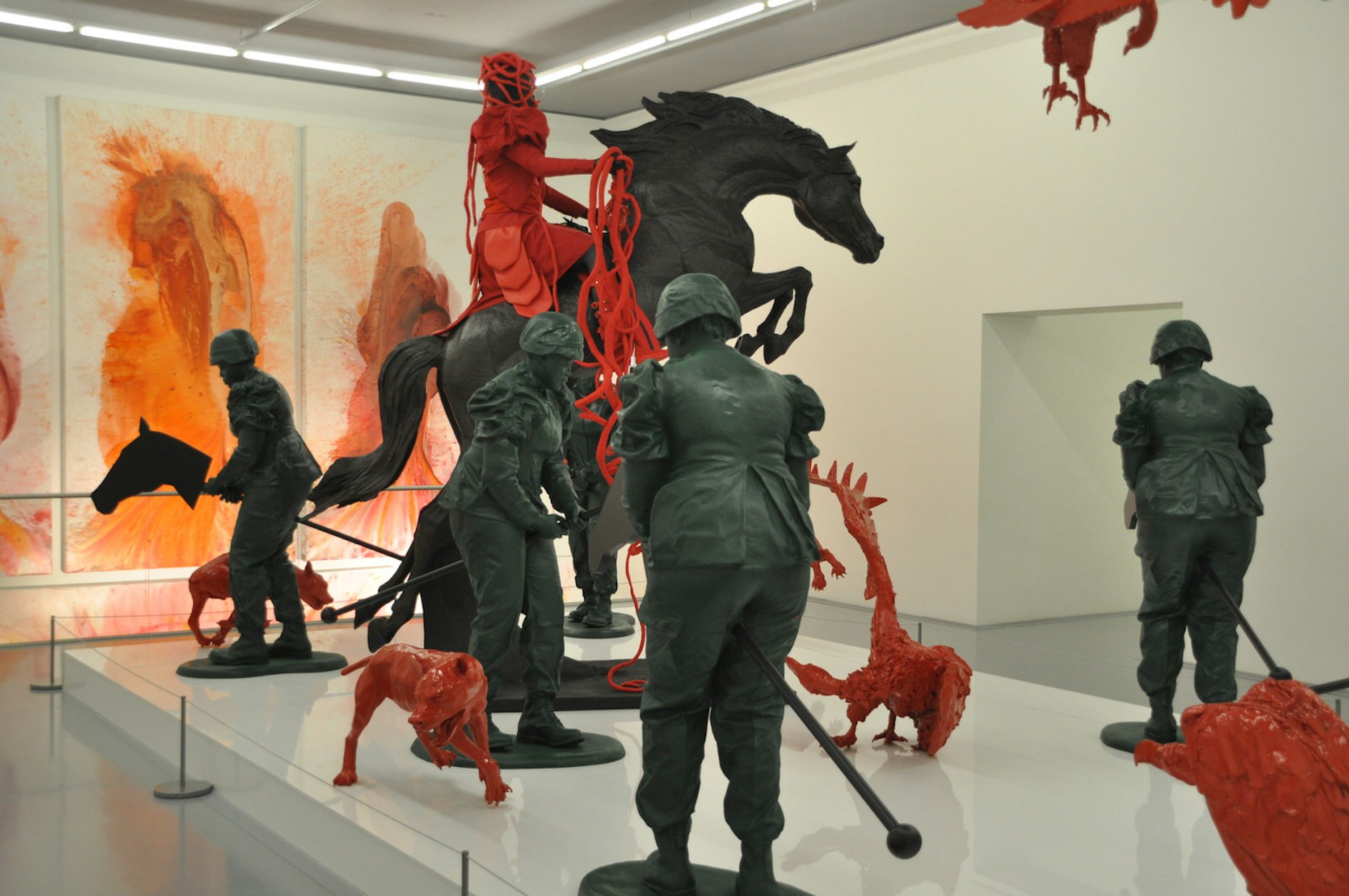 Copper statues of modern soldiers riding hobby horses stand amongst bright red vultures and dogs. One Roman-looking solider (also bright red) rides a life-sized copper horse that is rearing up on two legs © Monica Suma / Lonely Planet