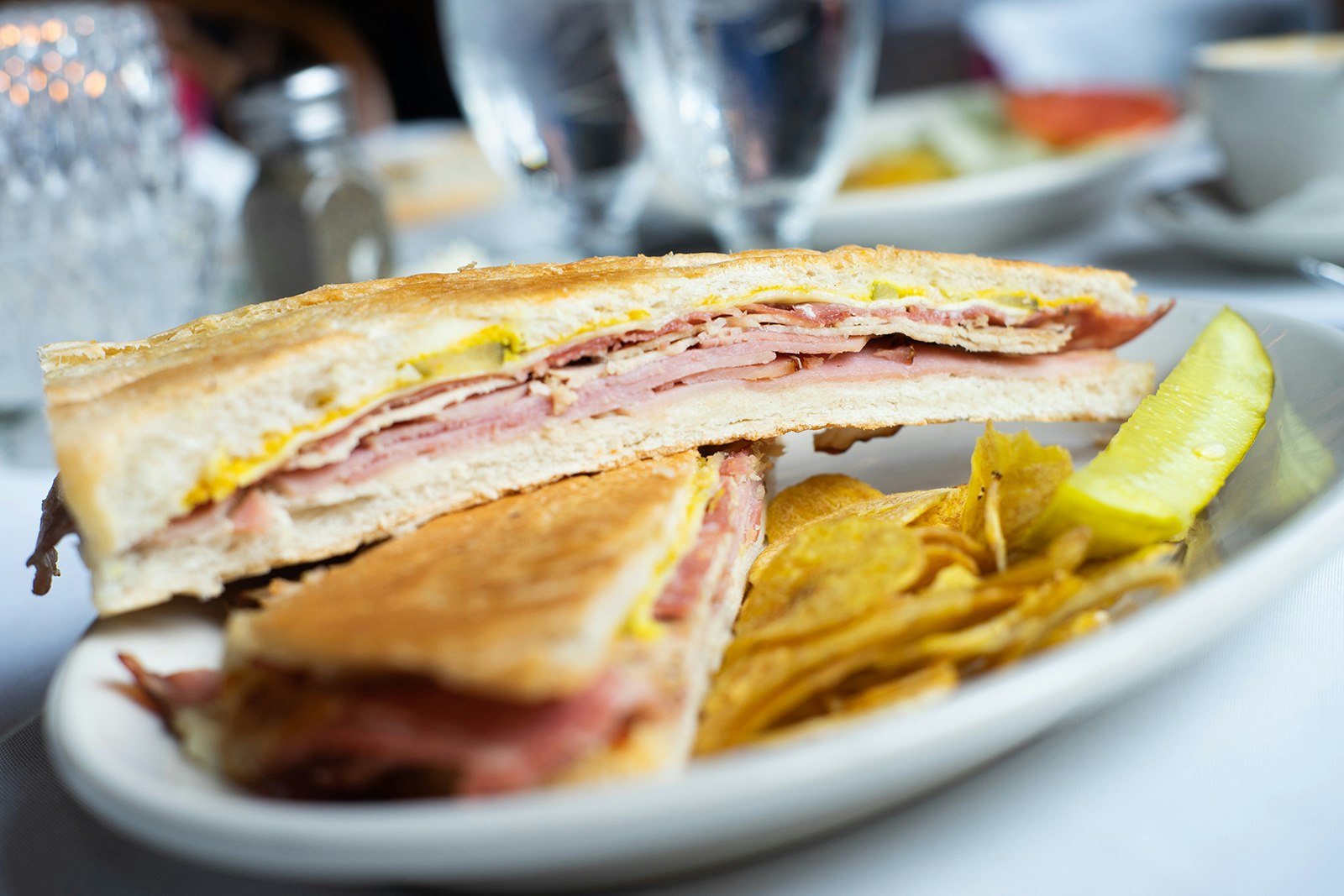 close-up shot of a sliced cuban sandwich with a pickle on a white plate © Dominic Cador / Lonely Planet