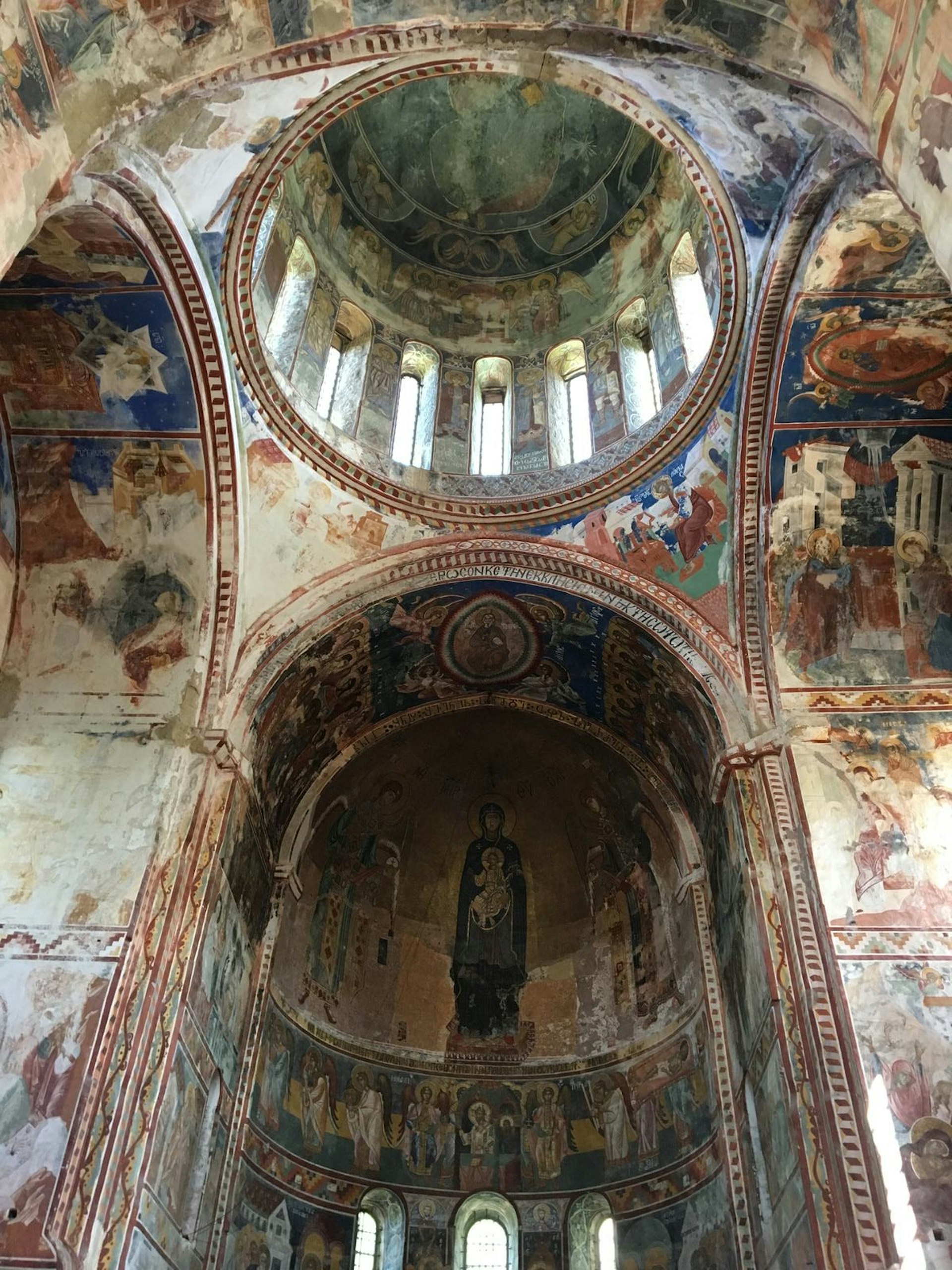 Upwards angle towards the dome inside Unesco-listed Gelati Monastery, showing colourful religious frescoes preserved on the walls and ceilings inside