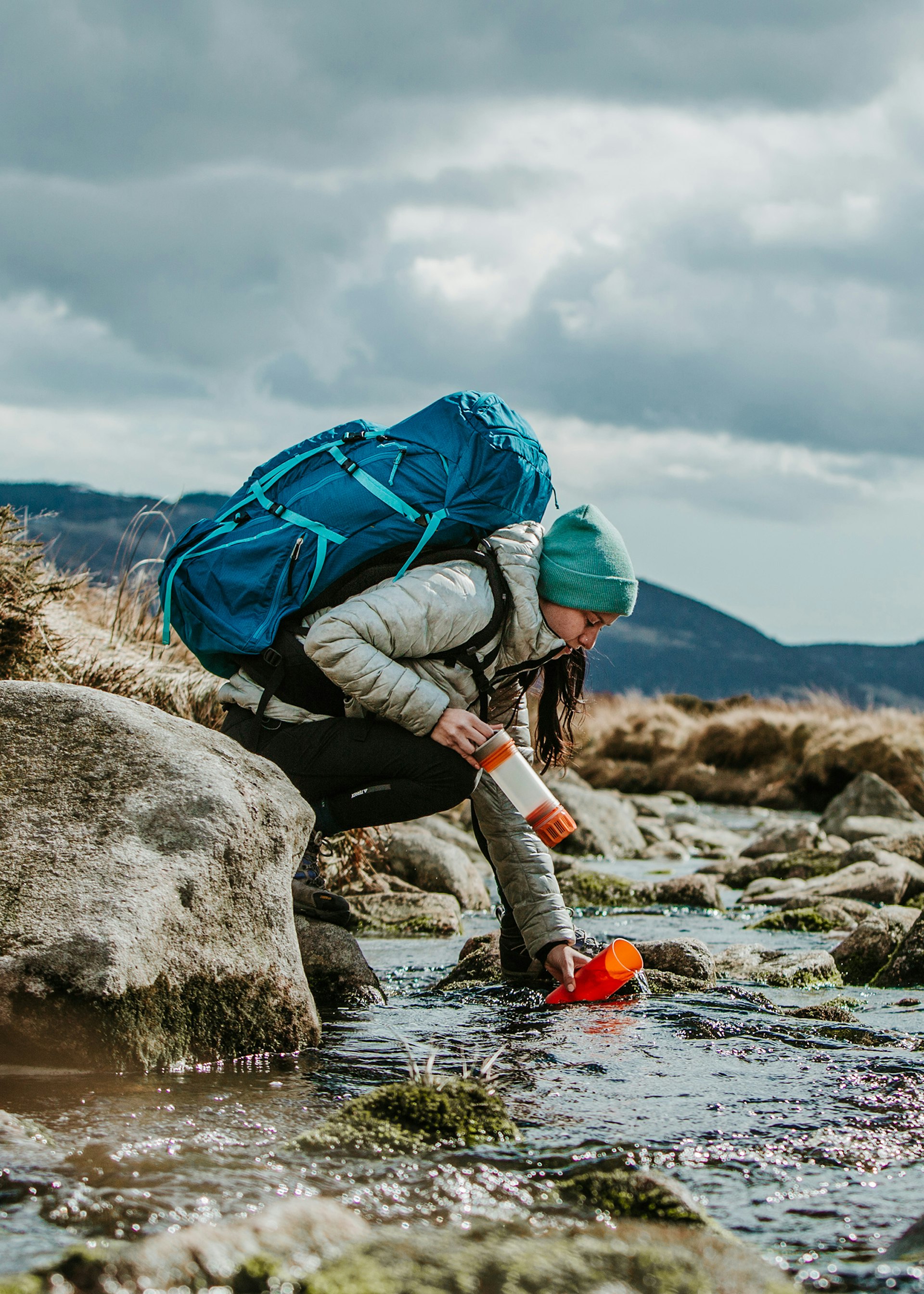 A female hiker filling her GRAYL bottle in a stream © GRAYL