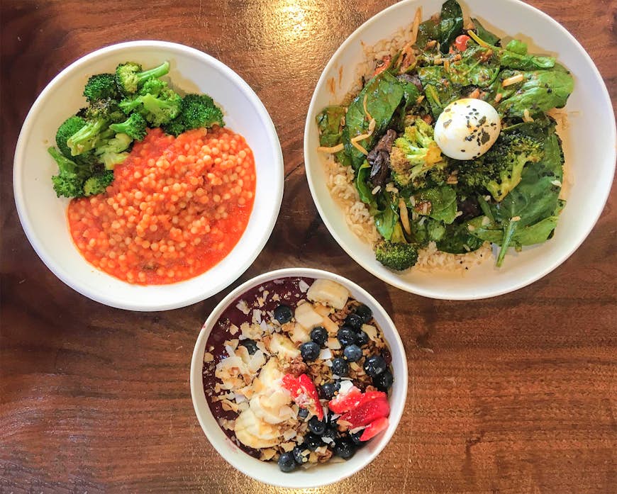 Aerial view of three bowl-style meals, one with lentils, a second with grains topped with greens and a seven-minute egg, and the third with acai covered in granola and fruit; healthy chicago