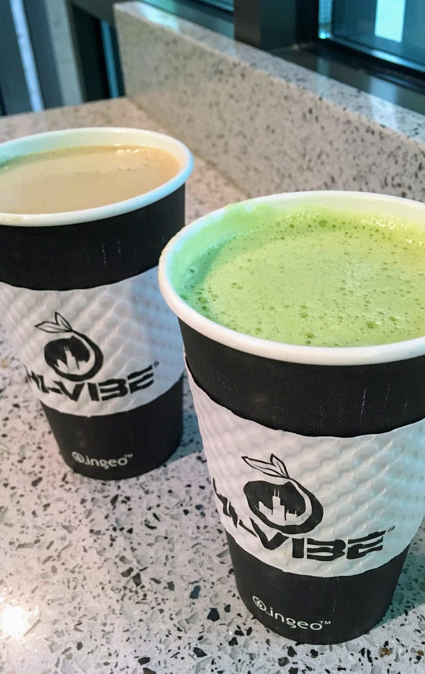 A cup of coffee and a vivid green matcha drink sit on a speckled marble counter inside Hi Vibe in Chicago; healthy chicago