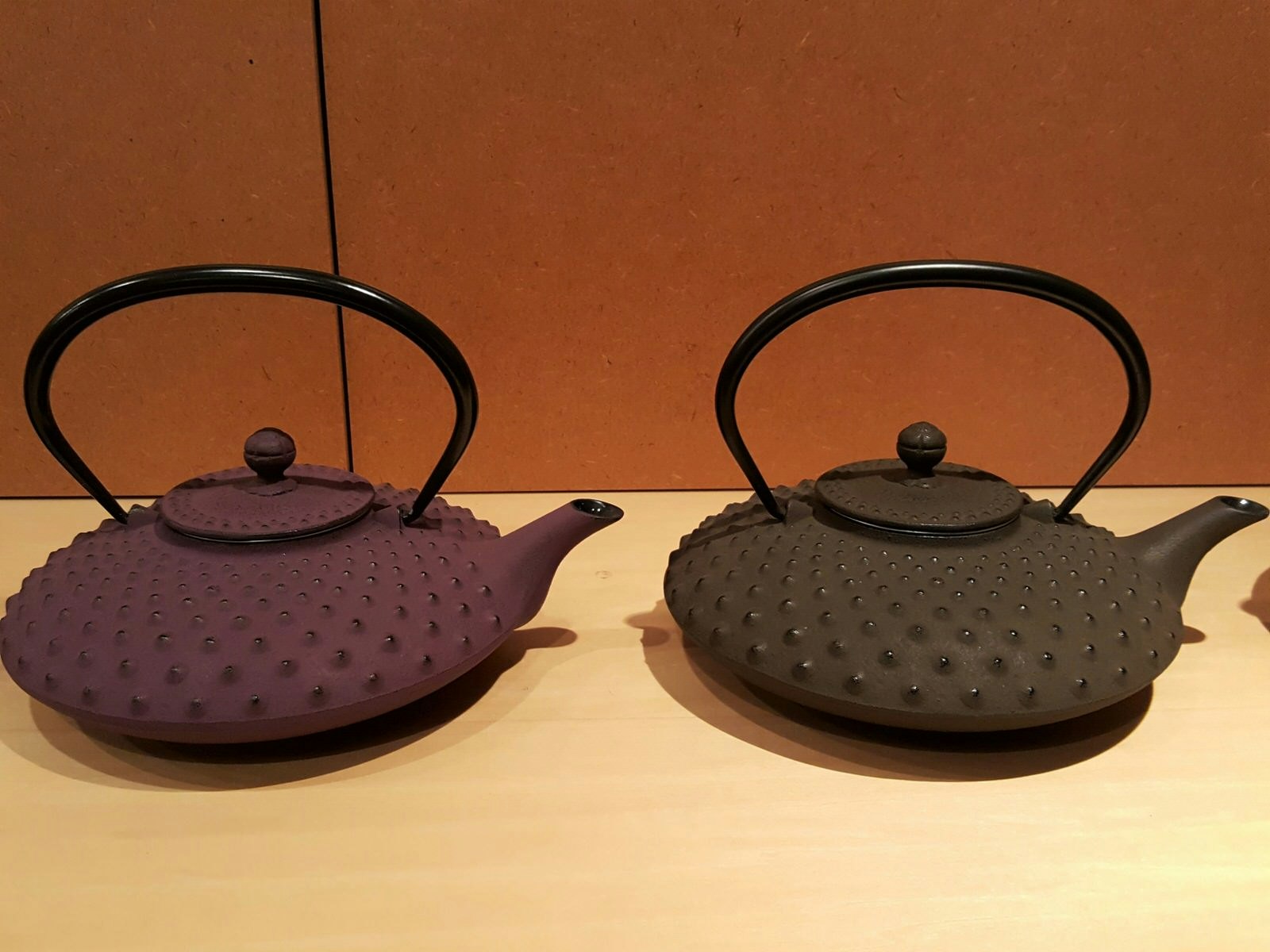 Two cast-iron tea kettles, one purple and one black, on a display shelf at Iwachu