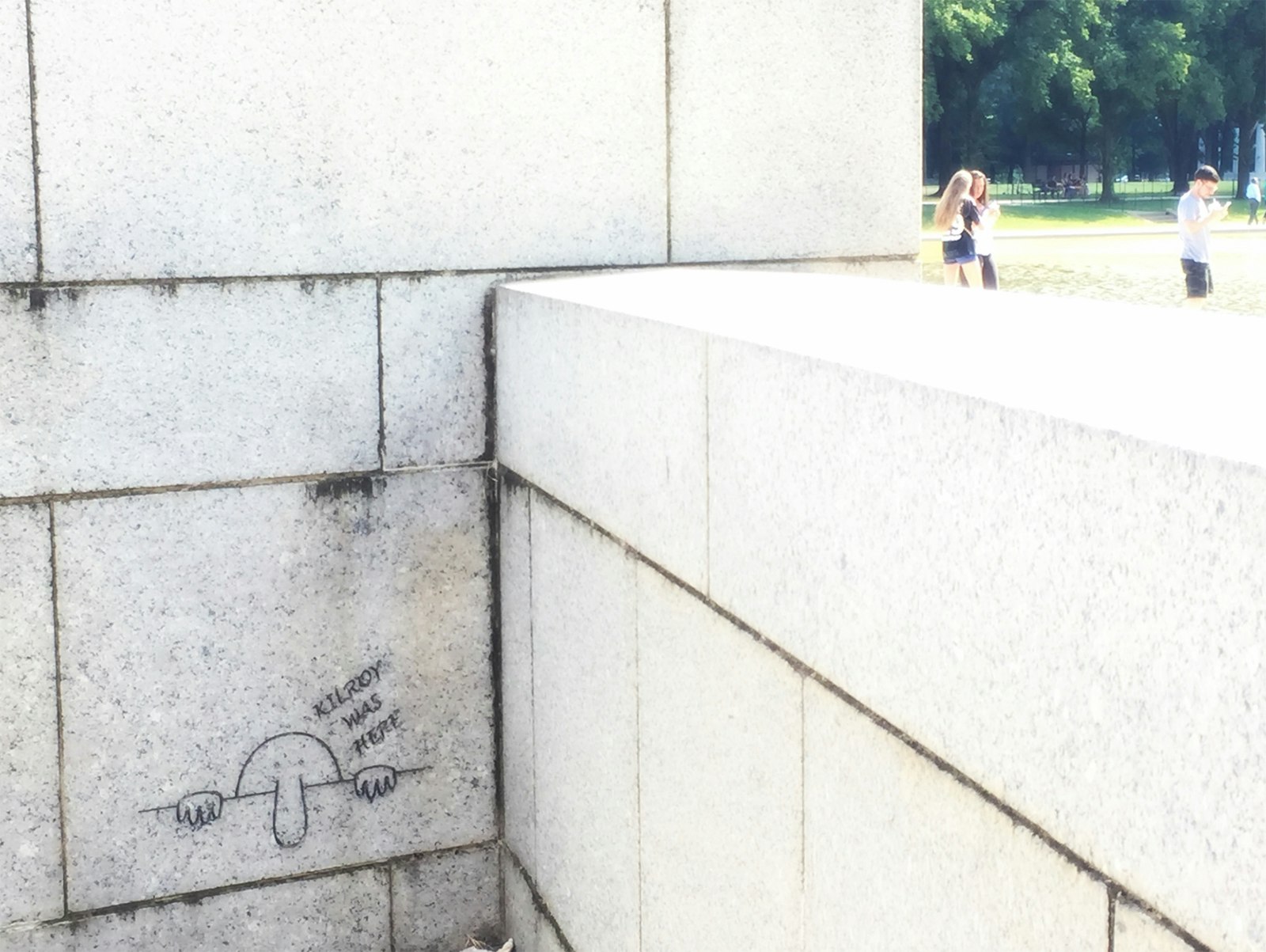 Close up of the white stone walls of the WWII Memorial in Washington DC, with a black line drawing of a man with a long nose peeking over a wall and the words 'Kilroy was here' © Barbara Noe Kennedy / Lonely Planet
