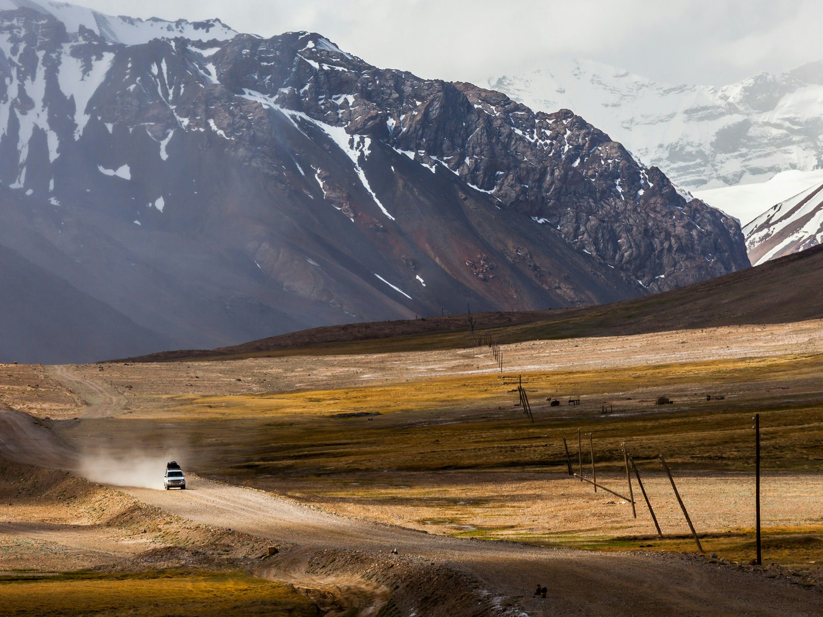 A 4WD drives down a dirt road through a valley surrounded by mountains. Chris's bucket list travel experience: a road trip down the Pamir Hwy through Tajikistan ©NOWAK LUKASZ/Shutterstock