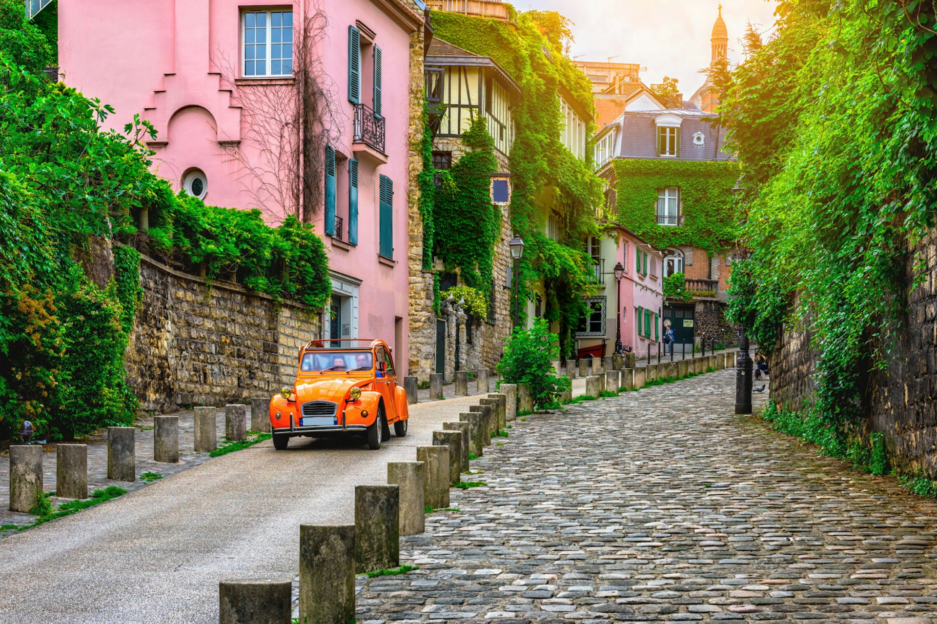 A red Citroen 2CV parked along an old cobbled street near a pink house in Montmartre, Paris © Catarina Belova / Shutterstock