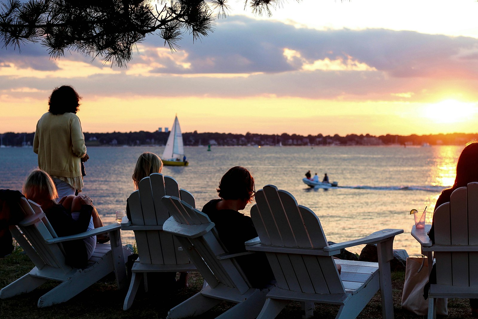 People sit in adirondack chairs on the beach in Rhode Island's Narragansett Bay, as the sun sets © Anna Saxon / Lonely Planet