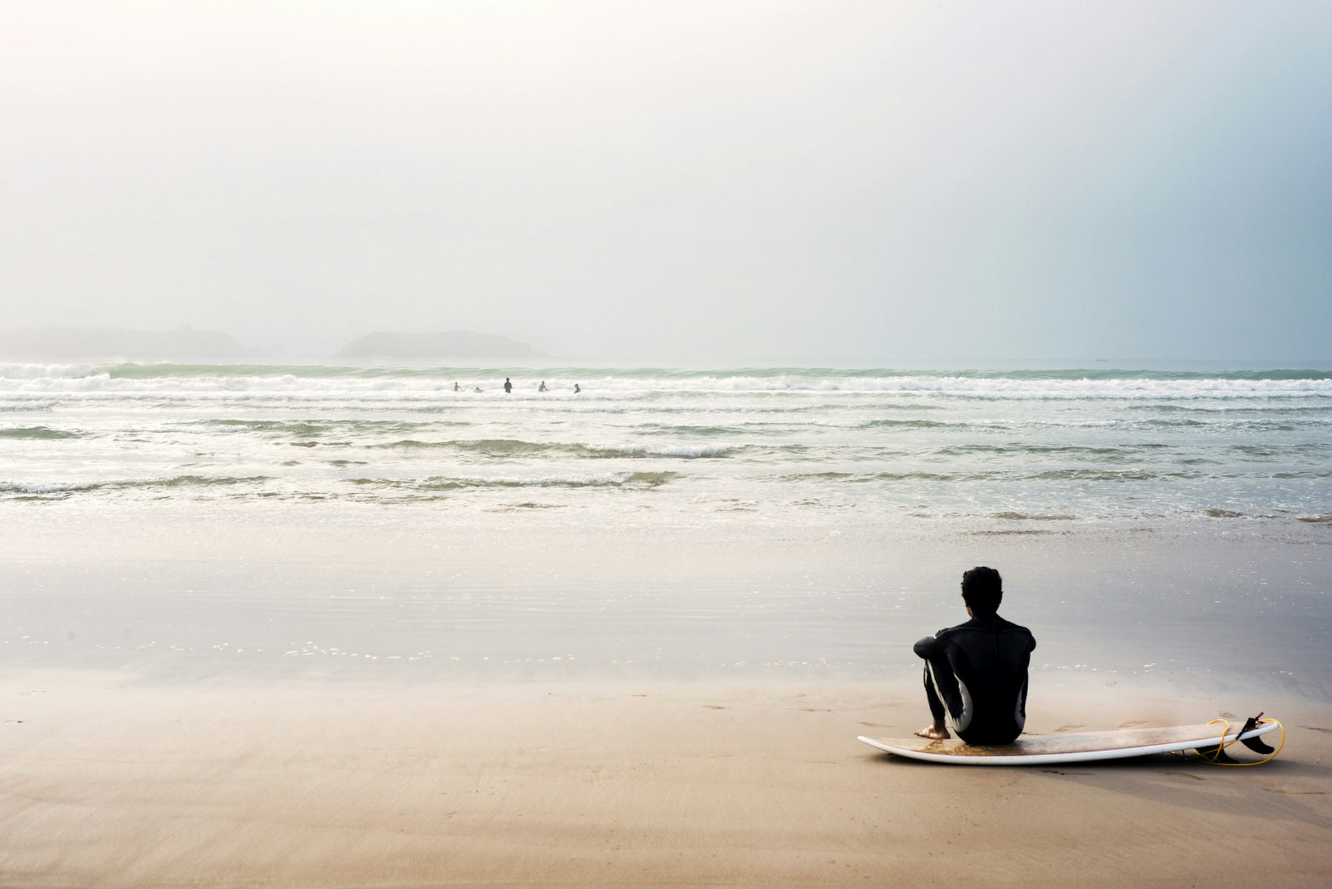 Man sitting on beach by surfboard © Hans Neleman / Getty Images
