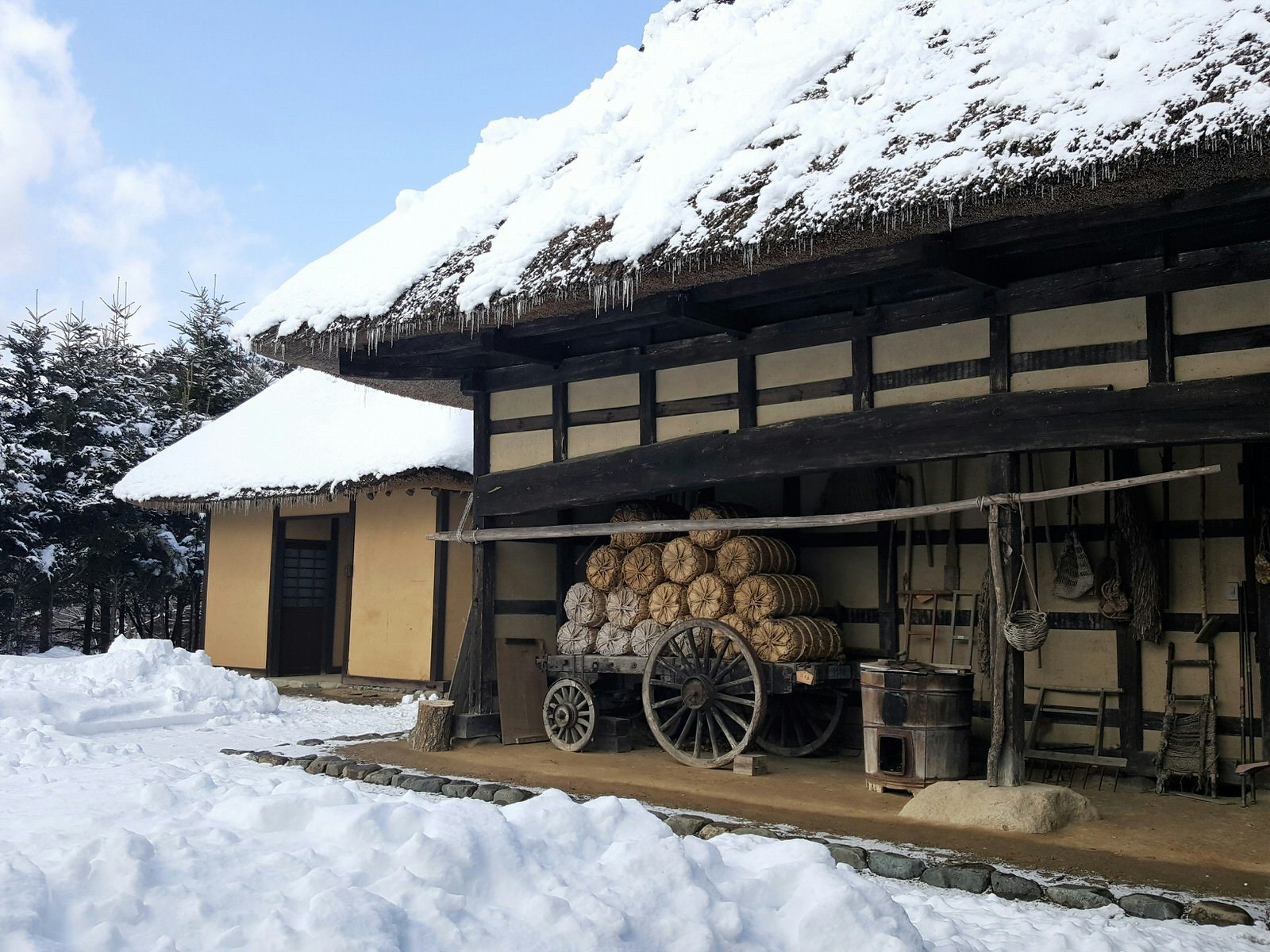 En gammal bondgård med halmtak med snö på taket och på marken utanför, vid Tono Furusato Village