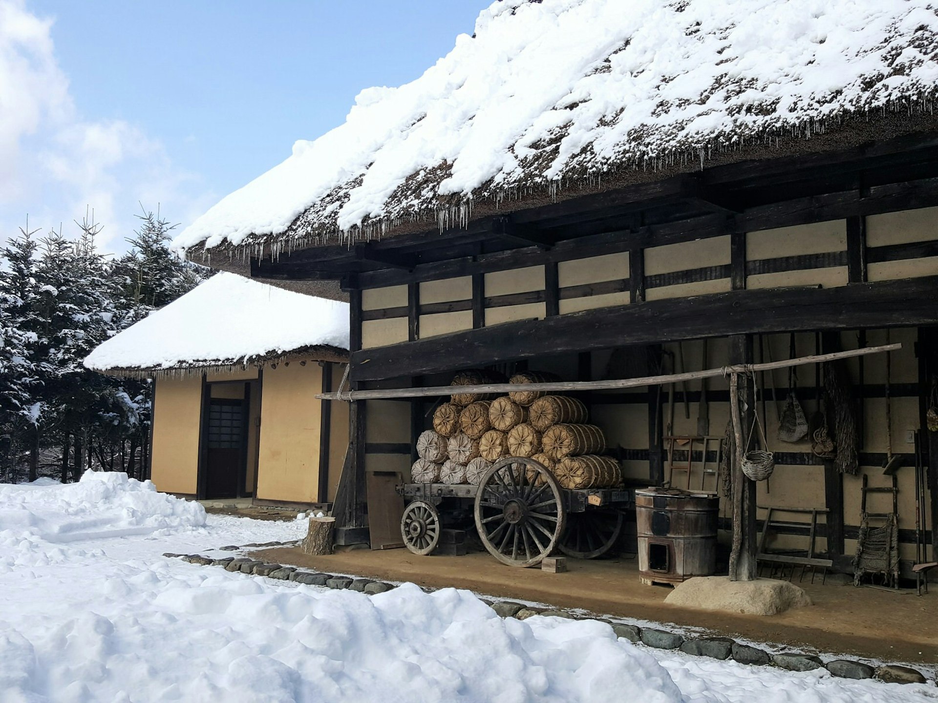 An old thatched-roof farmhouse with snow on the roof and on the ground outside, at Tono Furusato Village