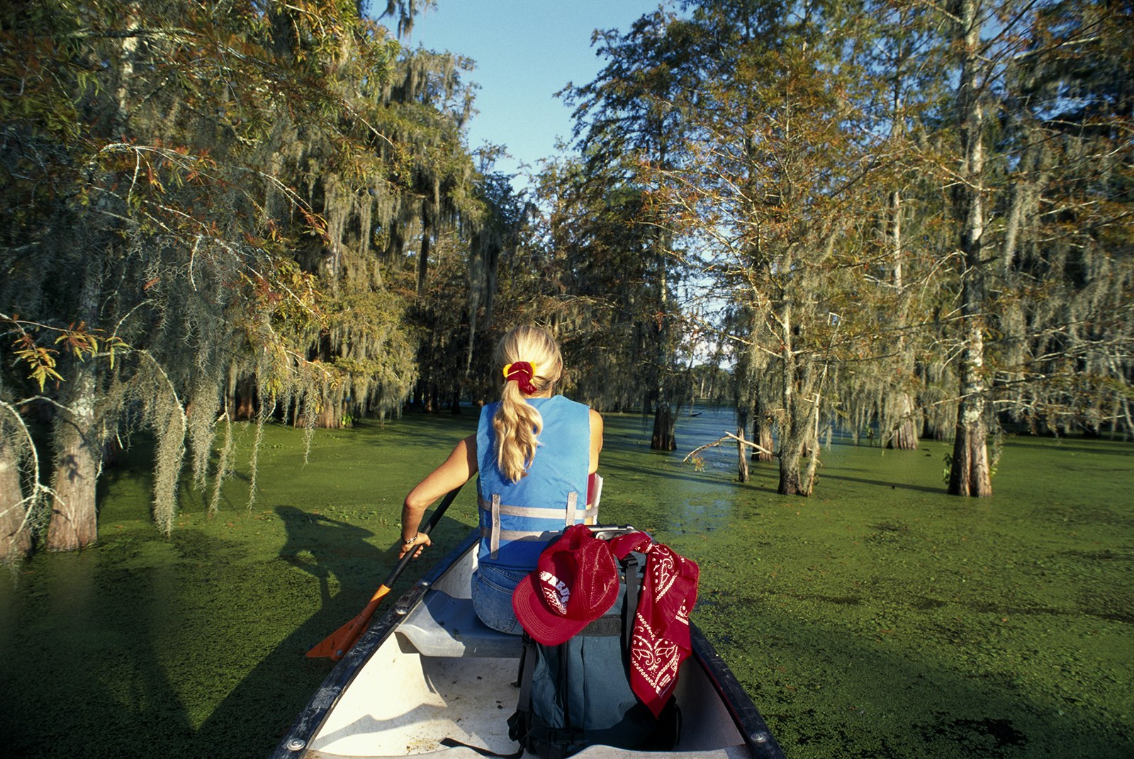 Posterior view of blonde woman in a life jacket kayaking through the green waters of a Louisiana swamp © Macduff Everton / Getty Images