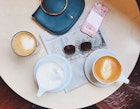 Mugs of coffee sit on a table along with a purse, sunglasses and a newspaper © Jessica Lam / Lonely Planet