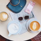 Mugs of coffee sit on a table along with a purse, sunglasses and a newspaper © Jessica Lam / Lonely Planet