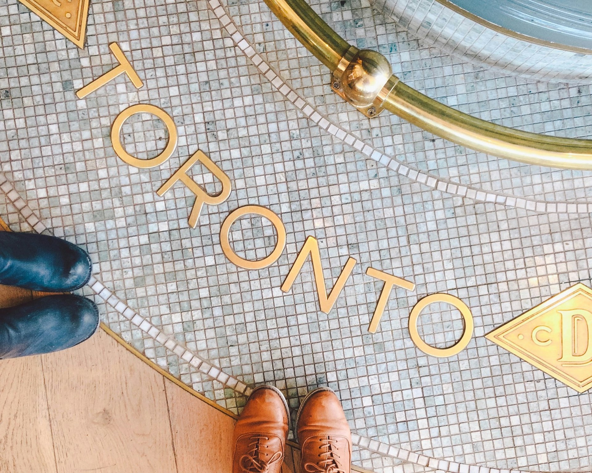 Two sets of feet are seen in front of a tile mosaic floor with the brass word 'Toronto' spelled out on top © Jessica Lam / Lonely Planet