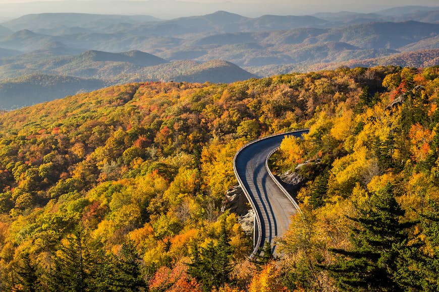 An elevated road snakes through dense woodland of colorful fall foliage along the Blue Ridge Parkway, North Carolina